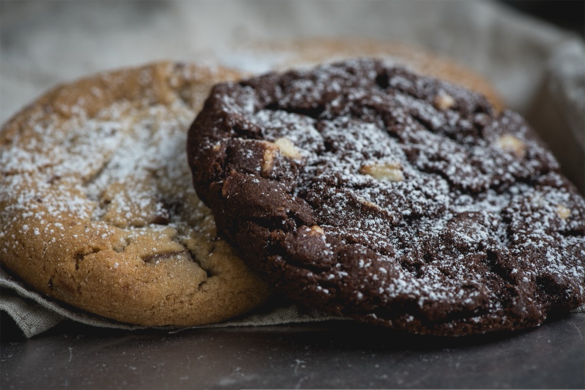 A chocolate cookie resting on a plain cookie, both dusted with powdered sugar.